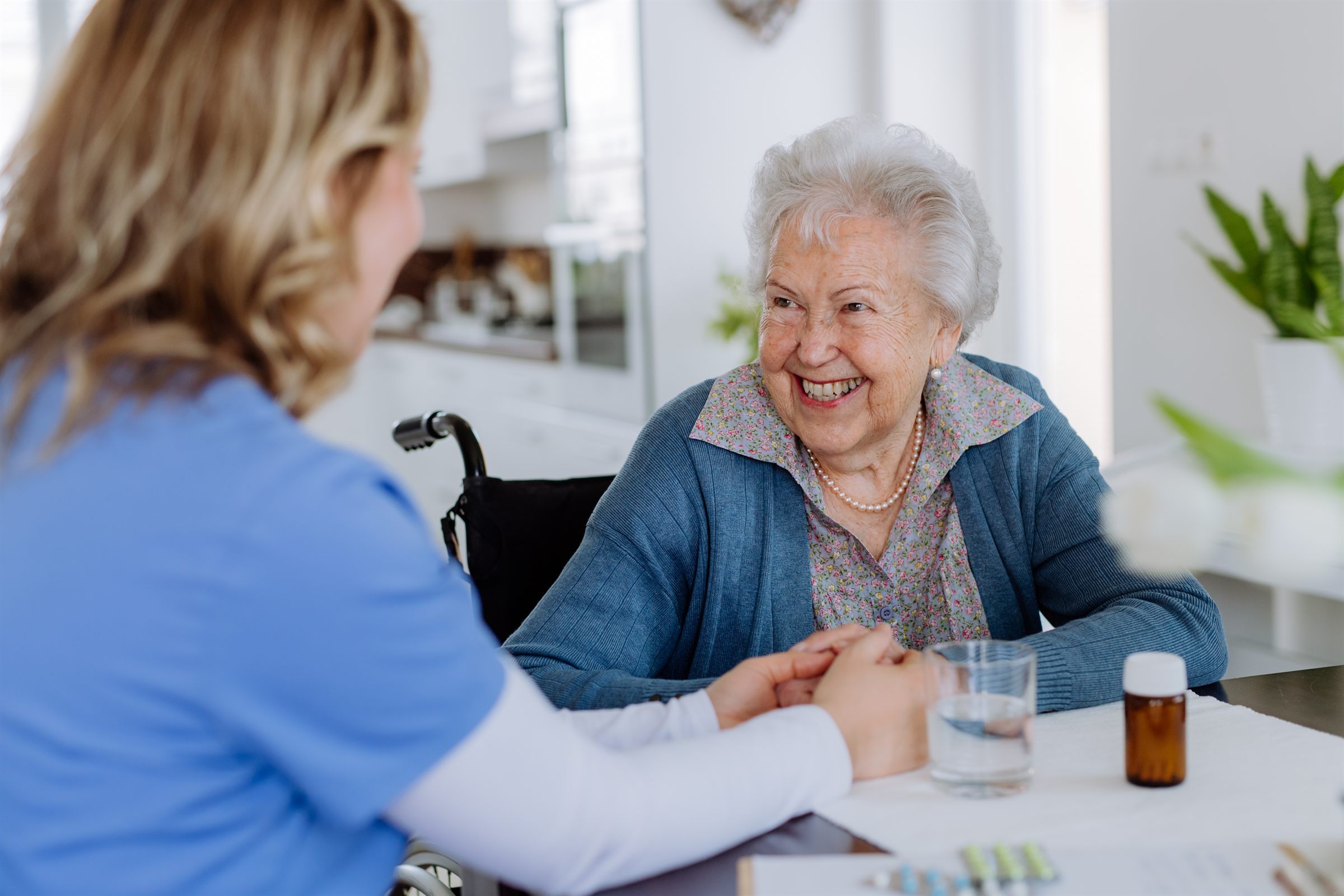 Carer holding hands with elderly woman in wheelchair